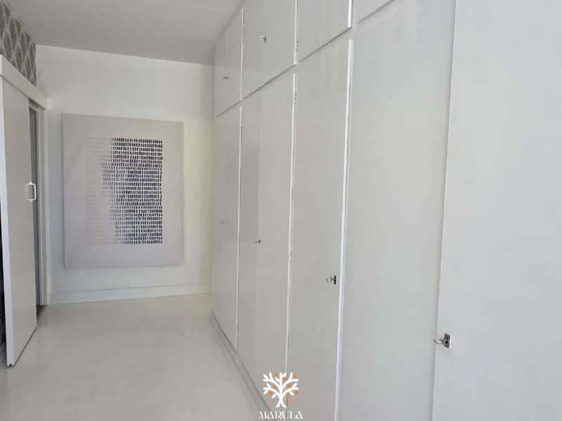 A bright, minimalist hallway featuring extensive built-in floor-to-ceiling storage cabinetry and a clean, neutral aesthetic.