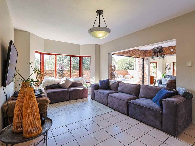 Spacious living room featuring tiled flooring, a large bay window, and seamless access to an outdoor patio area through sliding glass doors.