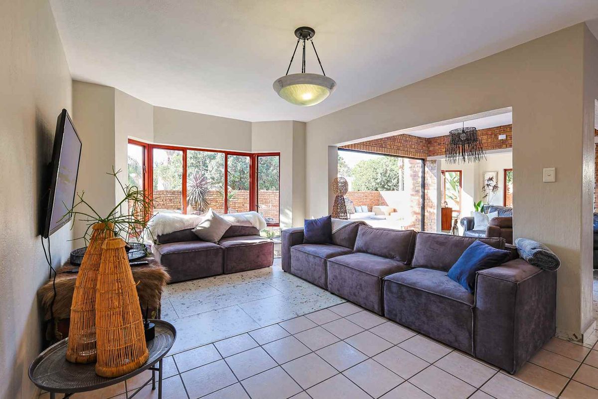 Spacious living room featuring tiled flooring, a large bay window, and seamless access to an outdoor patio area through sliding glass doors.