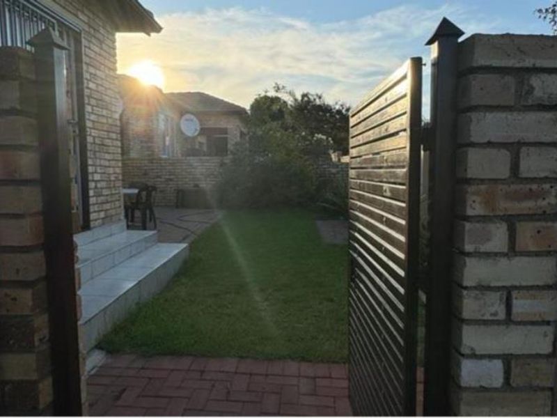 View of the townhouse entrance featuring a brick boundary wall, metal gate, paved walkway, and tiled steps leading to the facebrick facade.