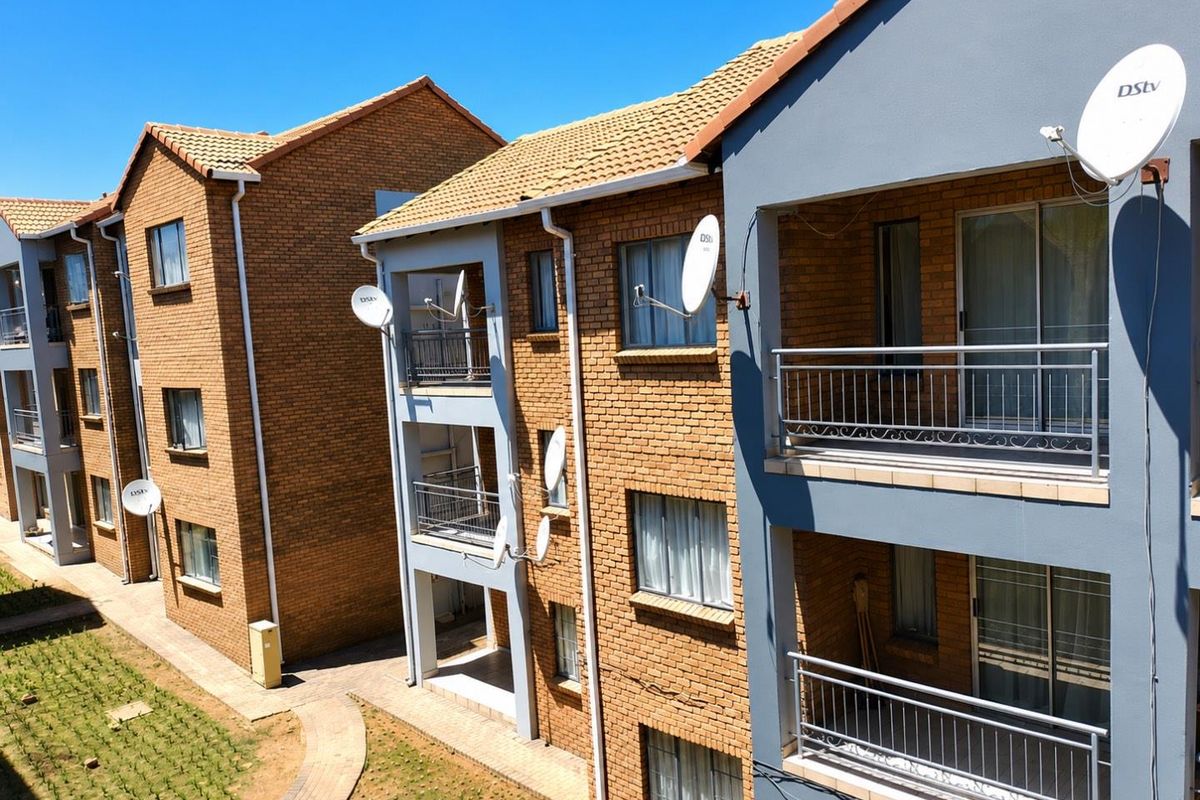 Exterior view of a multi-story apartment complex featuring face-brick facades, tiled roofs, and private balconies with metal railings.
