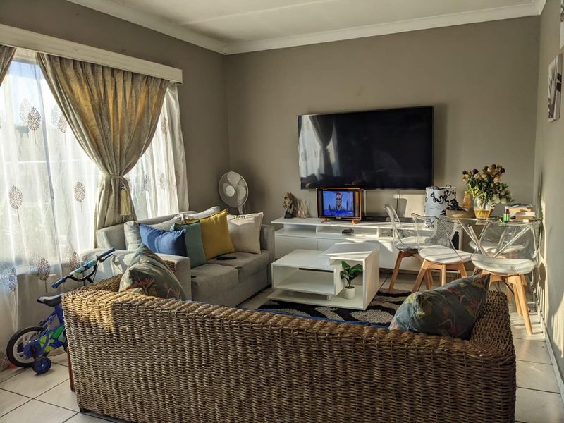 A comfortable living room featuring tiled flooring, neutral wall tones, and a large window that allows for ample natural light.