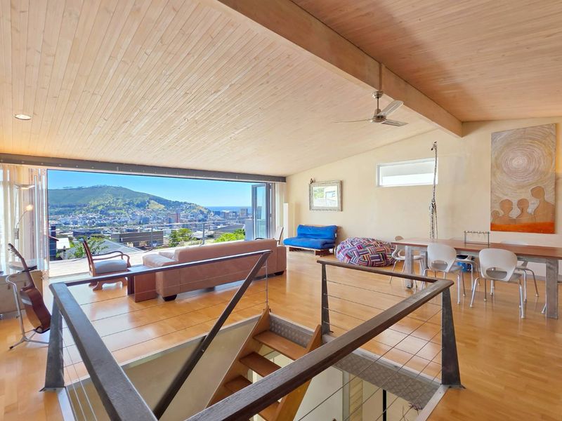 Spacious open-plan living and dining area featuring high timber vaulted ceilings, hardwood floors, and expansive folding glass doors opening to panoramic city and mountain views.