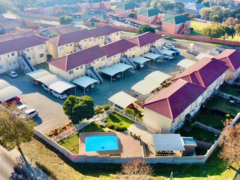 Aerial view of an apartment complex featuring multiple residential blocks, covered parking bays, a communal swimming pool, and perimeter fencing.