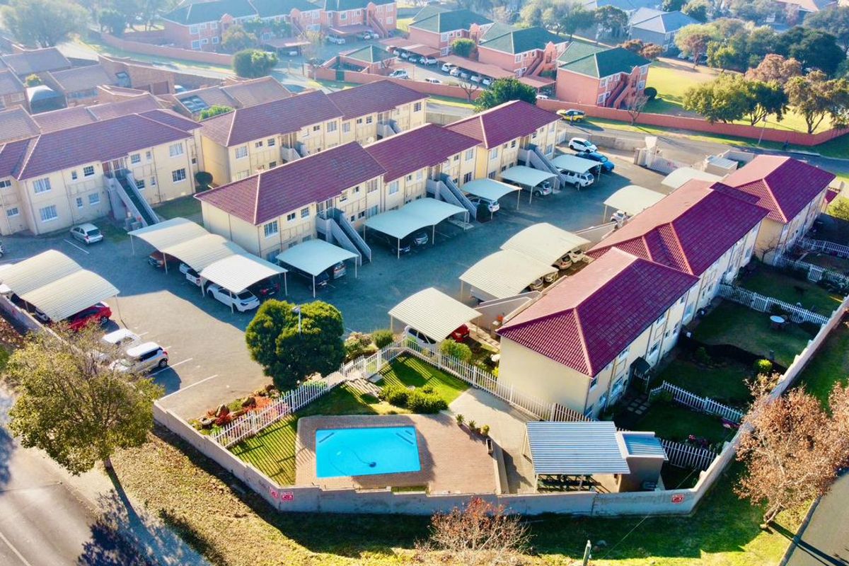 Aerial view of an apartment complex featuring multiple residential blocks, covered parking bays, a communal swimming pool, and perimeter fencing.