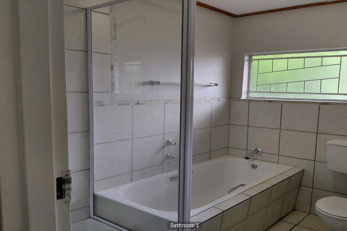 A functional bathroom featuring a built-in bathtub with a glass shower screen, tiled walls, and a standard toilet and basin.