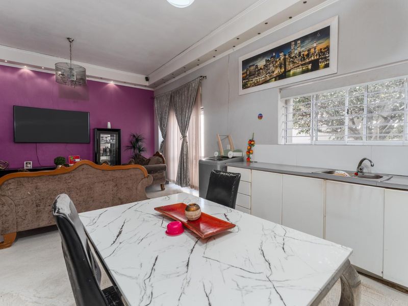 Open-plan living and kitchen area featuring built-in cabinetry, a stainless steel sink, and recessed lighting, with a distinct purple accent wall.