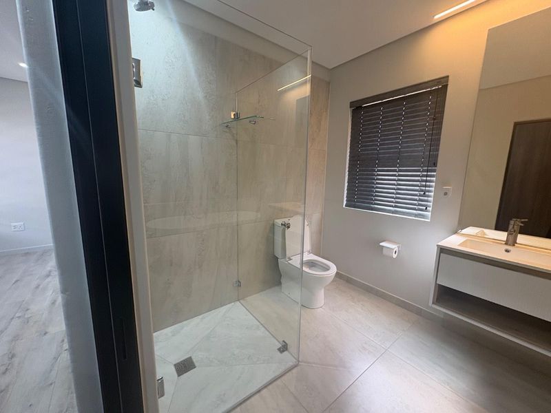 Modern bathroom featuring a glass-enclosed shower, wall-mounted toilet, and a sleek vanity cabinet with a basin.