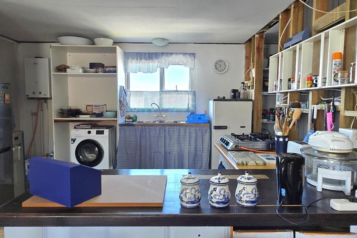 A rustic kitchen area featuring an open-shelf design, exposed wall framing, a built-in sink, and a gas cooktop, requiring significant renovation and finishing.
