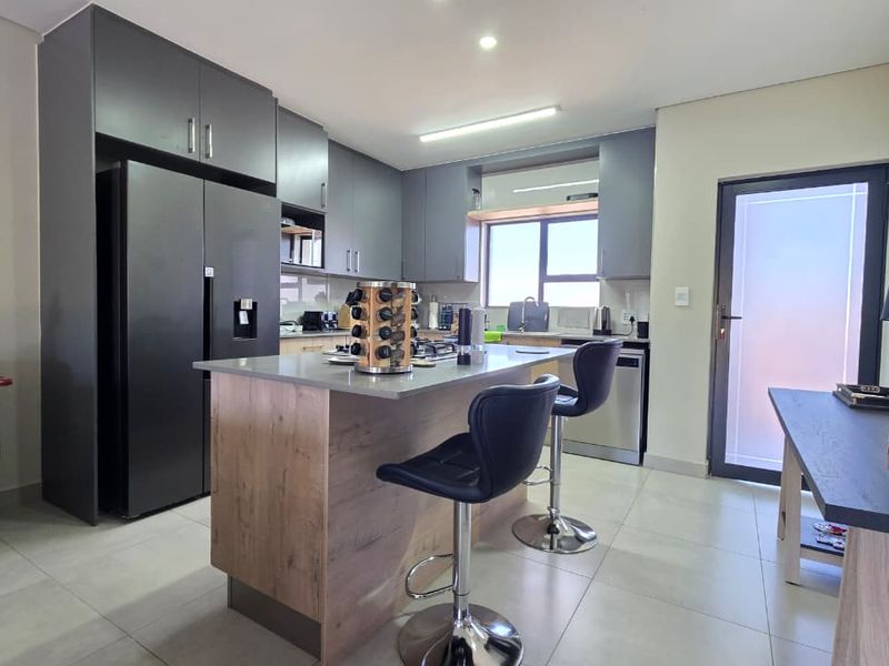 Modern kitchen featuring dark cabinetry, a central island with stone countertops, integrated appliances, and tiled flooring, offering a sleek and functional cooking space.