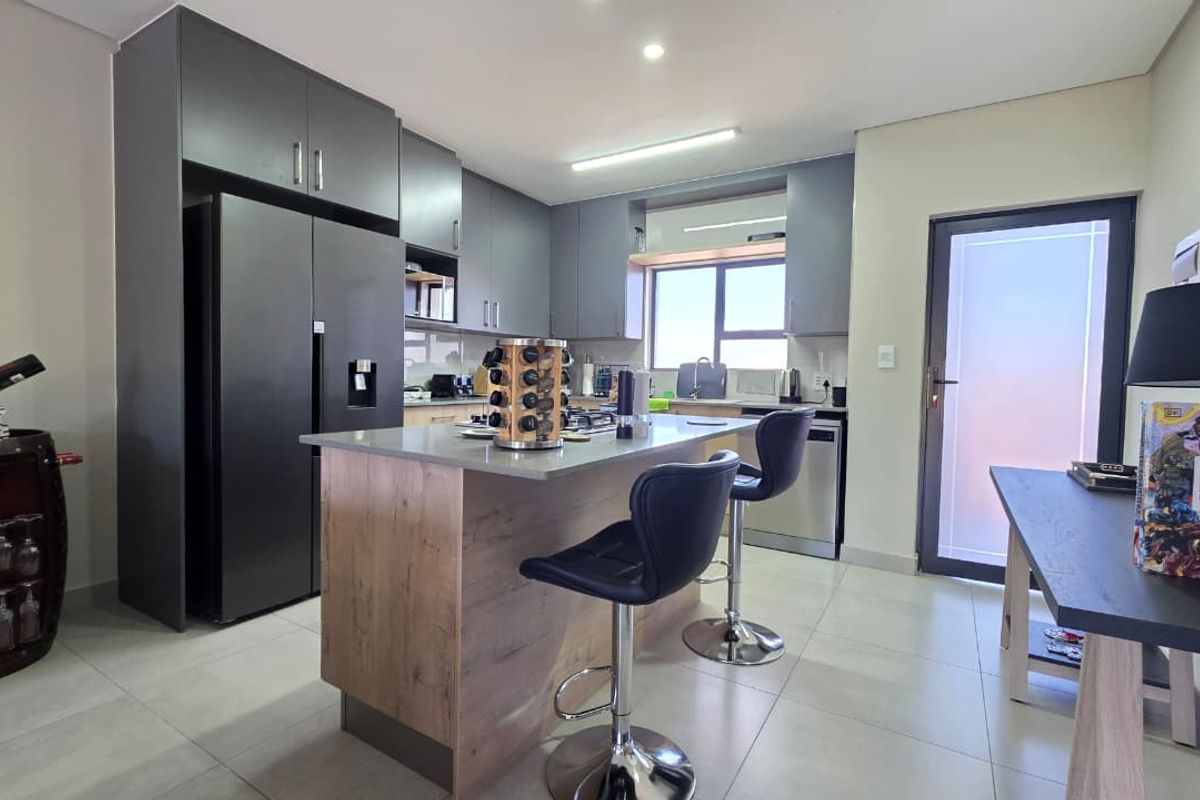 Modern kitchen featuring dark cabinetry, a central island with stone countertops, integrated appliances, and tiled flooring, offering a sleek and functional cooking space.