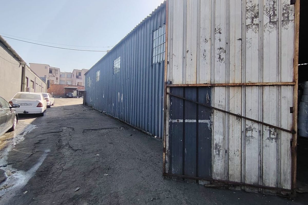 Exterior view of an industrial warehouse facility featuring corrugated metal siding, a large sliding gate, and an adjacent asphalt driveway.