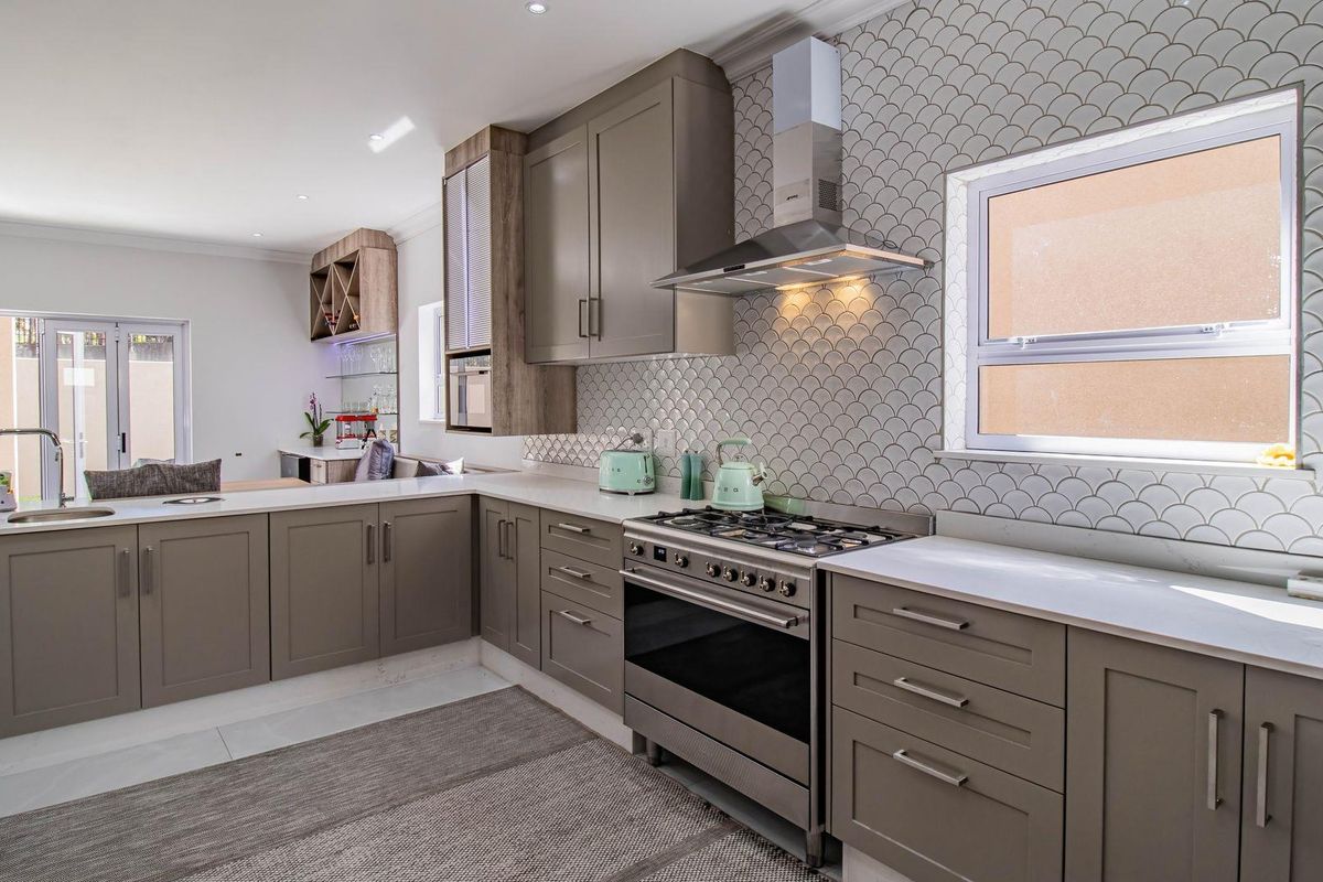 Modern kitchen featuring grey shaker-style cabinetry, quartz countertops, a gas stove with extractor fan, and a stylish scalloped tile backsplash.