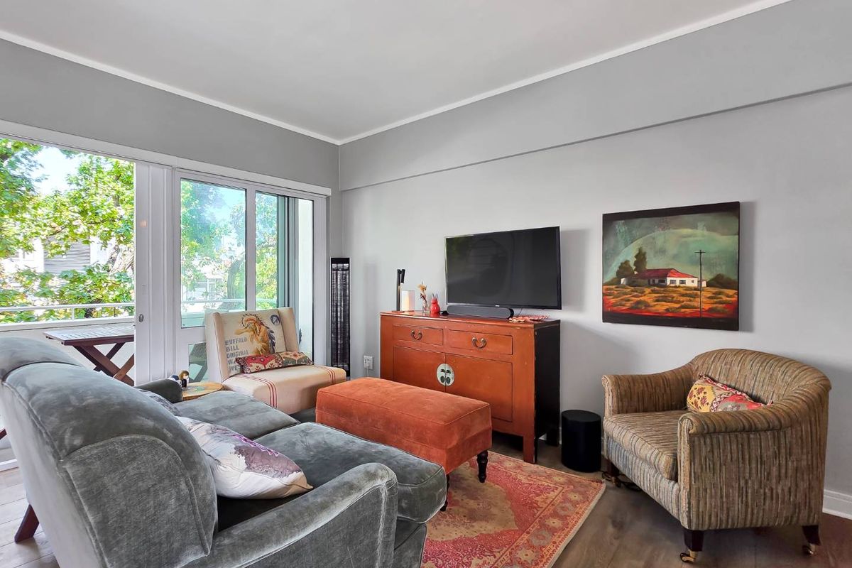 A well-maintained living room featuring laminate flooring, neutral wall tones, and a large sliding glass door providing access to an outdoor balcony area.