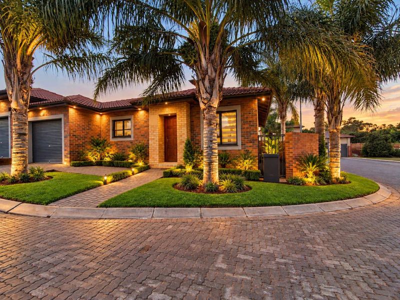 A beautifully presented brick facade home featuring a paved driveway, manicured garden, and warm exterior lighting at dusk.