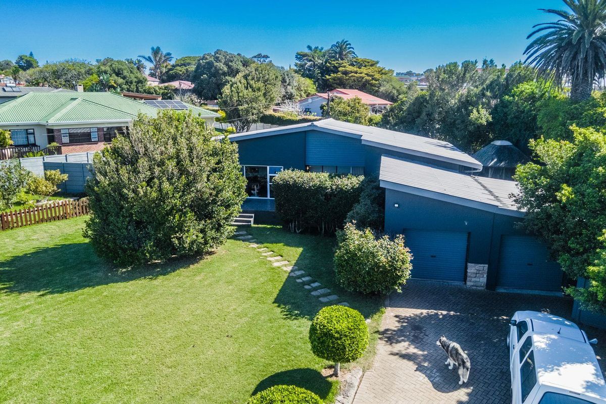Aerial view of a modern residential property featuring a double garage, paved driveway, and a well-maintained garden with mature trees.