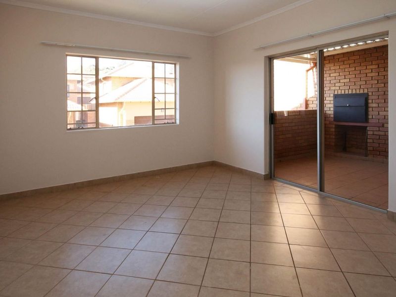 An empty, well-lit living room featuring neutral tiled flooring and a sliding glass door that opens onto a private patio area.