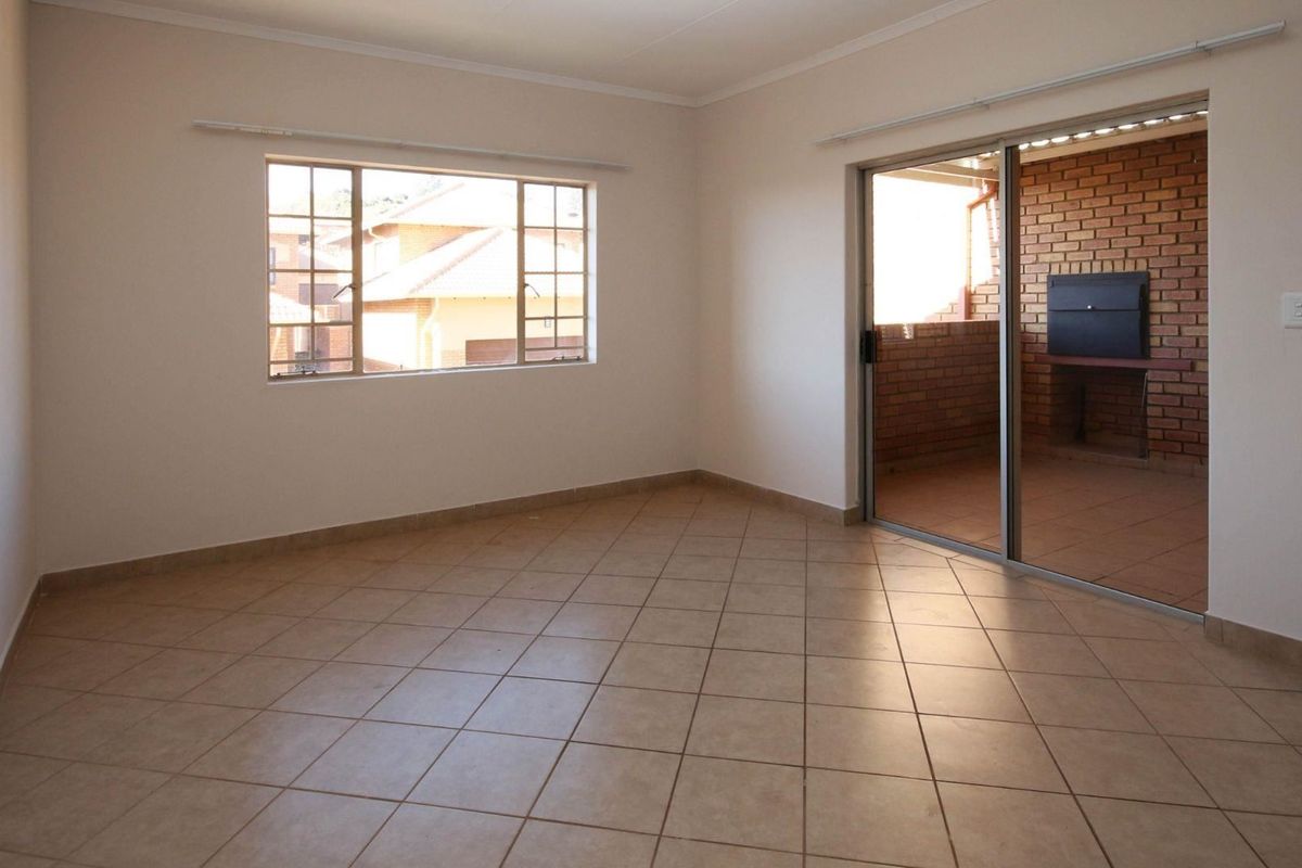 An empty, well-lit living room featuring neutral tiled flooring and a sliding glass door that opens onto a private patio area.