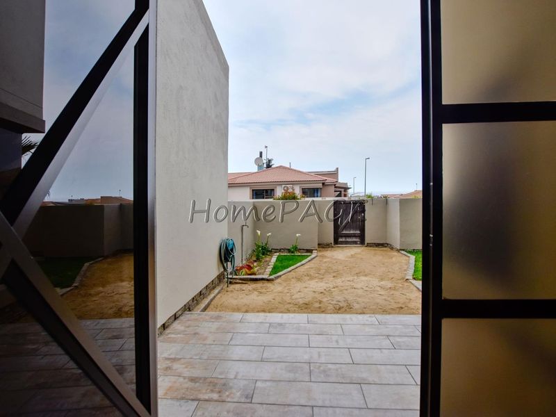 View from an interior space onto a tiled rear patio and an unfinished garden area with boundary walls.