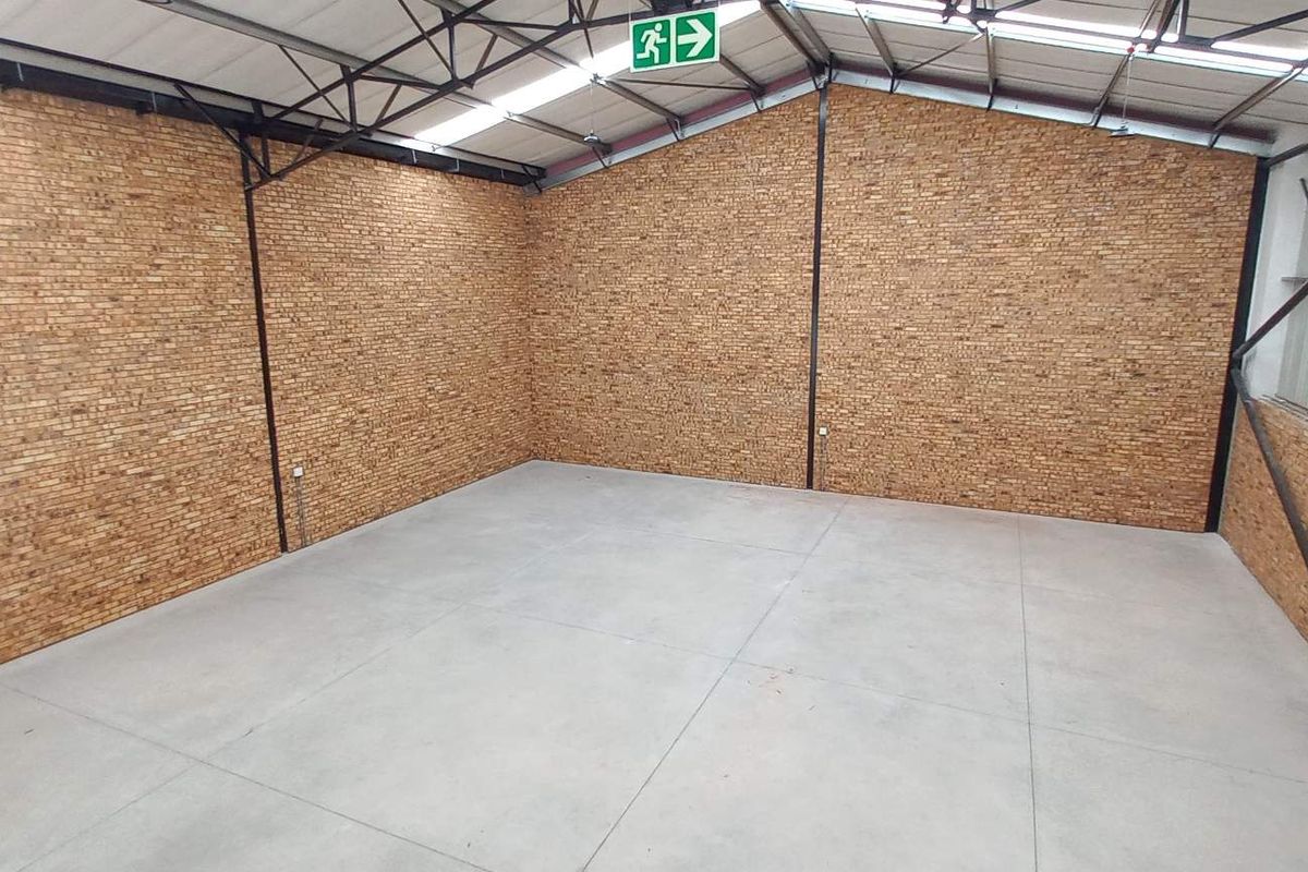 A spacious, empty industrial utility area featuring exposed brick walls, polished concrete flooring, and high-clearance steel roof trusses with natural lighting.