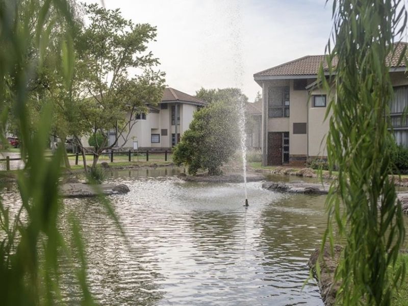 A scenic view of the apartment complex grounds featuring a central pond with a fountain and well-maintained landscaped surroundings.