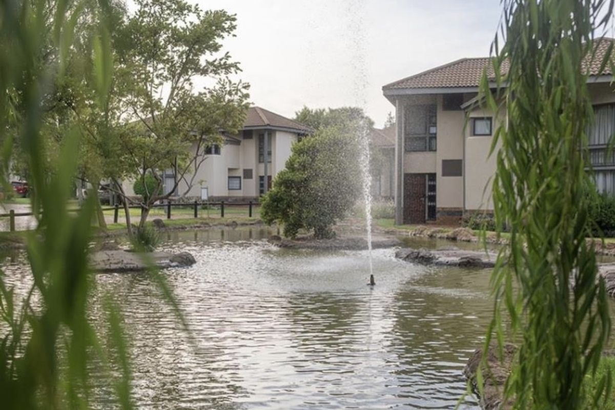 A scenic view of the apartment complex grounds featuring a central pond with a fountain and well-maintained landscaped surroundings.