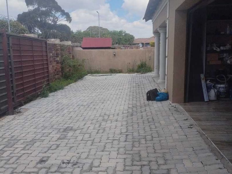 Rear exterior area featuring paved driveway, boundary wall, and access to the garage.