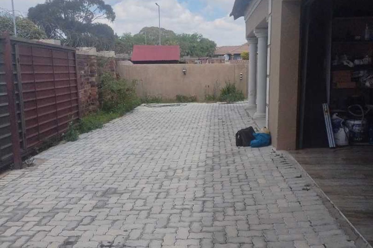 Rear exterior area featuring paved driveway, boundary wall, and access to the garage.