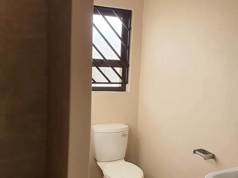 A functional bathroom featuring a tiled shower area, a standard toilet, and a window with security bars.