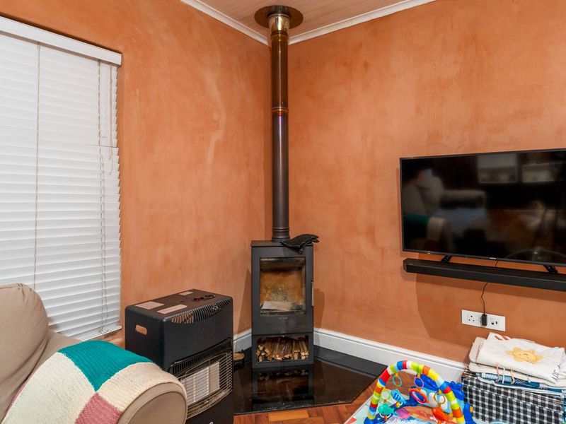 Living room featuring a corner wood-burning stove with a flue pipe, set against a textured orange wall with venetian blinds.