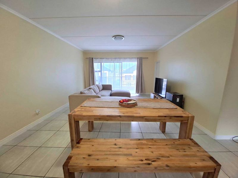 Open plan living and dining area featuring neutral tiled flooring and a sliding glass door leading to a balcony.