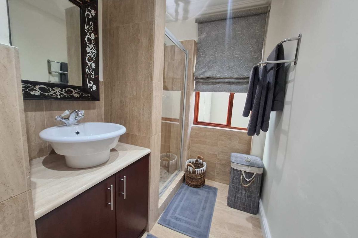A well-maintained bathroom featuring a modern vessel sink vanity, a glass-enclosed shower, and neutral floor-to-ceiling tiling.