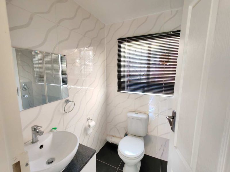 A clean and functional bathroom featuring a modern basin, vanity, toilet, and tiled finishes with natural light from a window with blinds.
