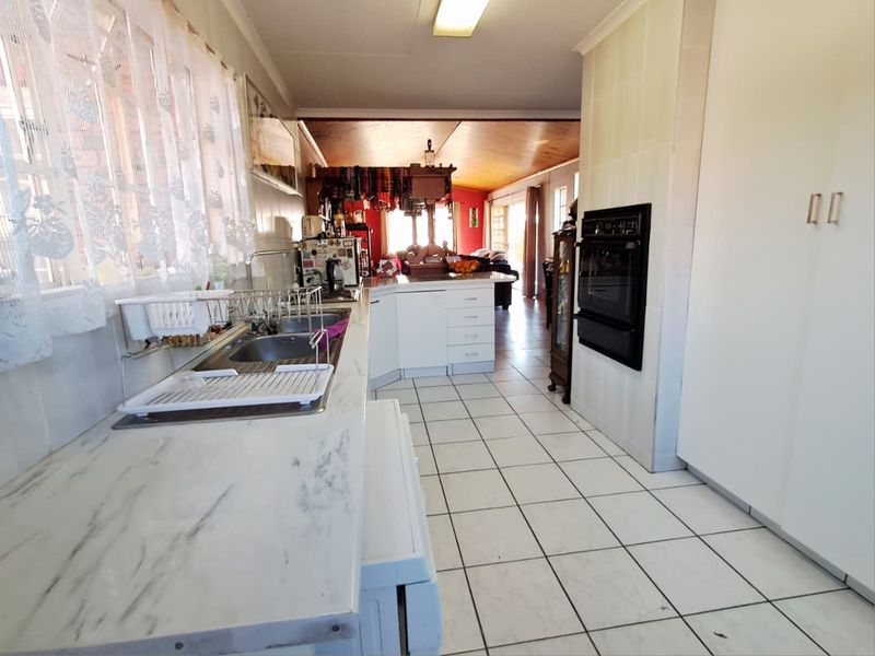 A functional kitchen featuring tiled flooring, laminate countertops, a double sink, and a built-in oven, with an open-plan layout leading to the living area.