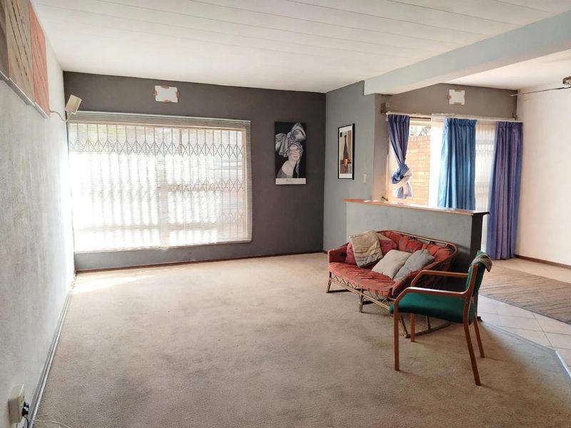 Spacious living area featuring a partition wall, security gates on windows, and ceiling fan, offering a versatile layout for comfortable family living.
