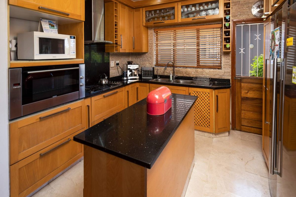 A functional kitchen featuring wooden cabinetry, black granite countertops, a central island, built-in oven, and a stainless steel extractor fan.