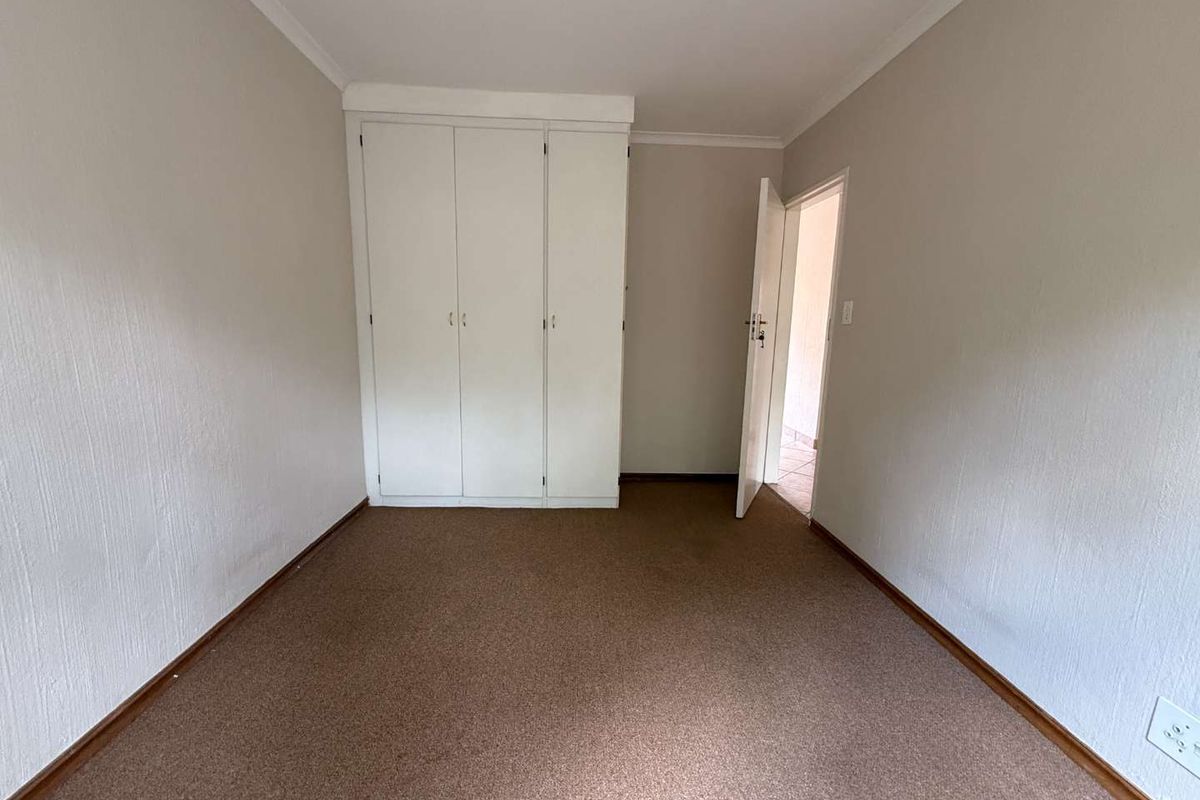 A vacant bedroom featuring built-in cupboards, neutral wall finishes, and carpeted flooring, offering a blank canvas for personalization.