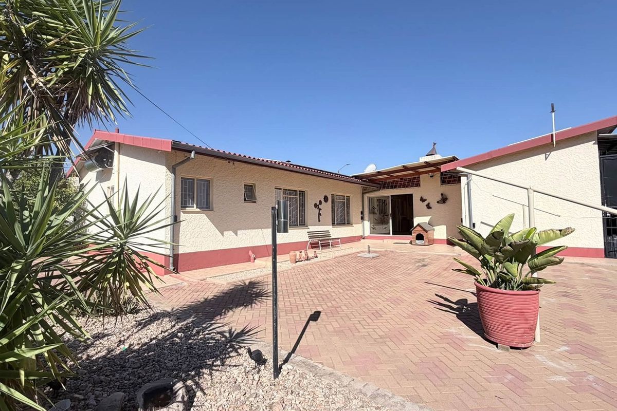 A rear exterior view of the house featuring a paved patio area, stucco walls, and a tiled roof under a clear blue sky.