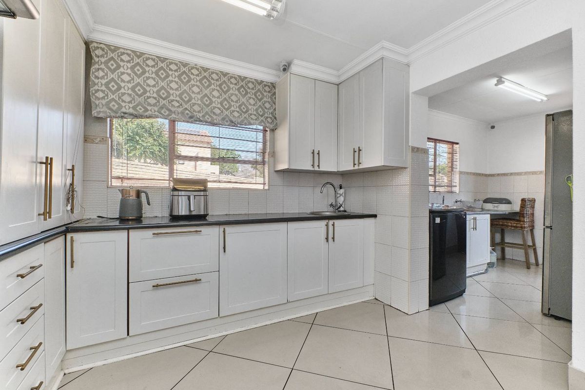 A functional kitchen featuring light-toned cabinetry, dark countertops, tiled backsplash, and ceramic flooring, with an adjacent scullery area visible.