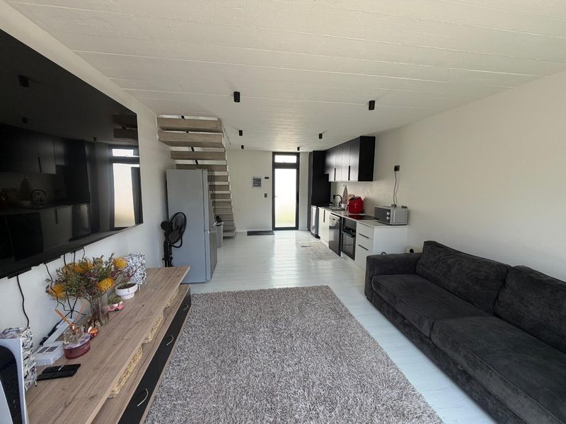 Modern open-plan living area featuring a sleek kitchen with built-in cabinetry, integrated appliances, and a staircase leading to the upper level.