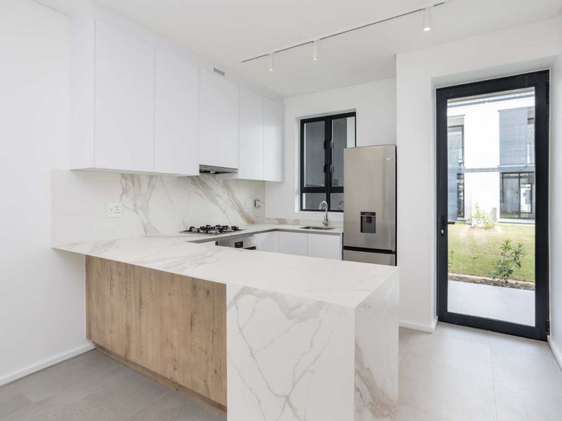 Modern kitchen featuring marble-look stone countertops, built-in gas hob, extractor fan, and direct access to the garden through a glass panel door.