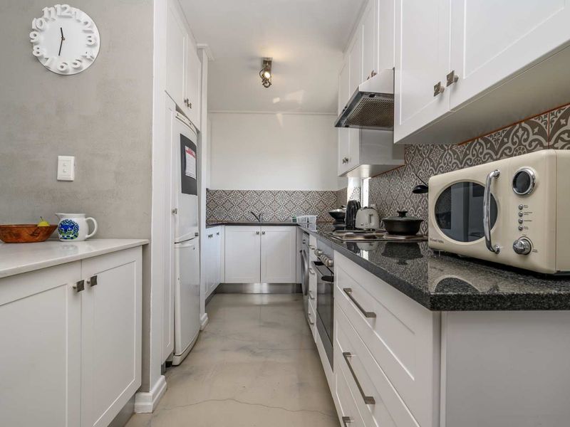 A well-maintained galley kitchen featuring white cabinetry, granite countertops, a decorative tile backsplash, and polished concrete flooring.
