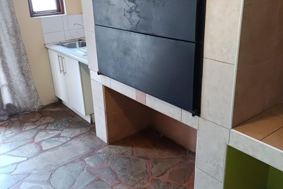 A kitchen area featuring a built-in braai, stone-style tiled flooring, and basic cabinetry with a sink.