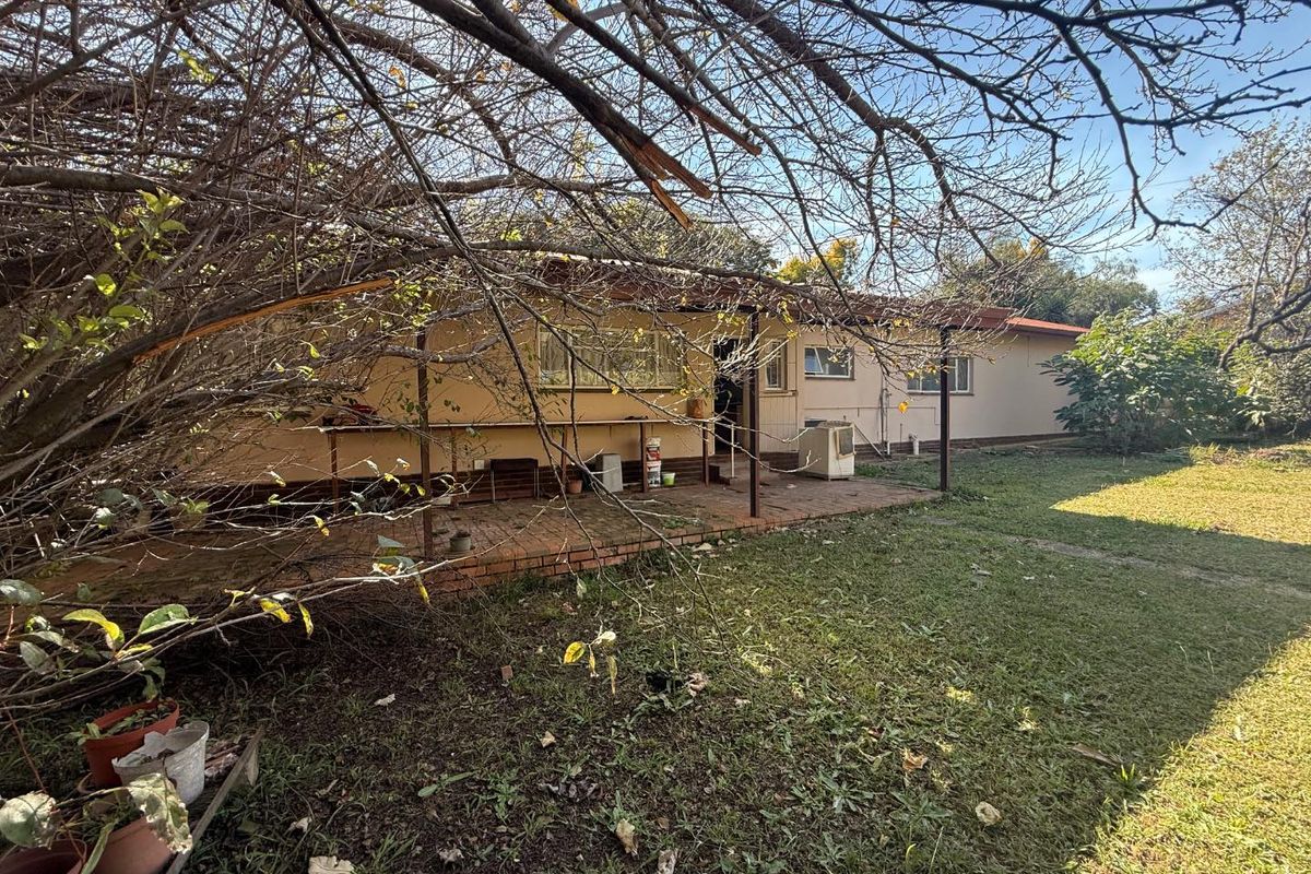 Rear view of the house featuring a covered brick patio area, established garden, and mature trees.
