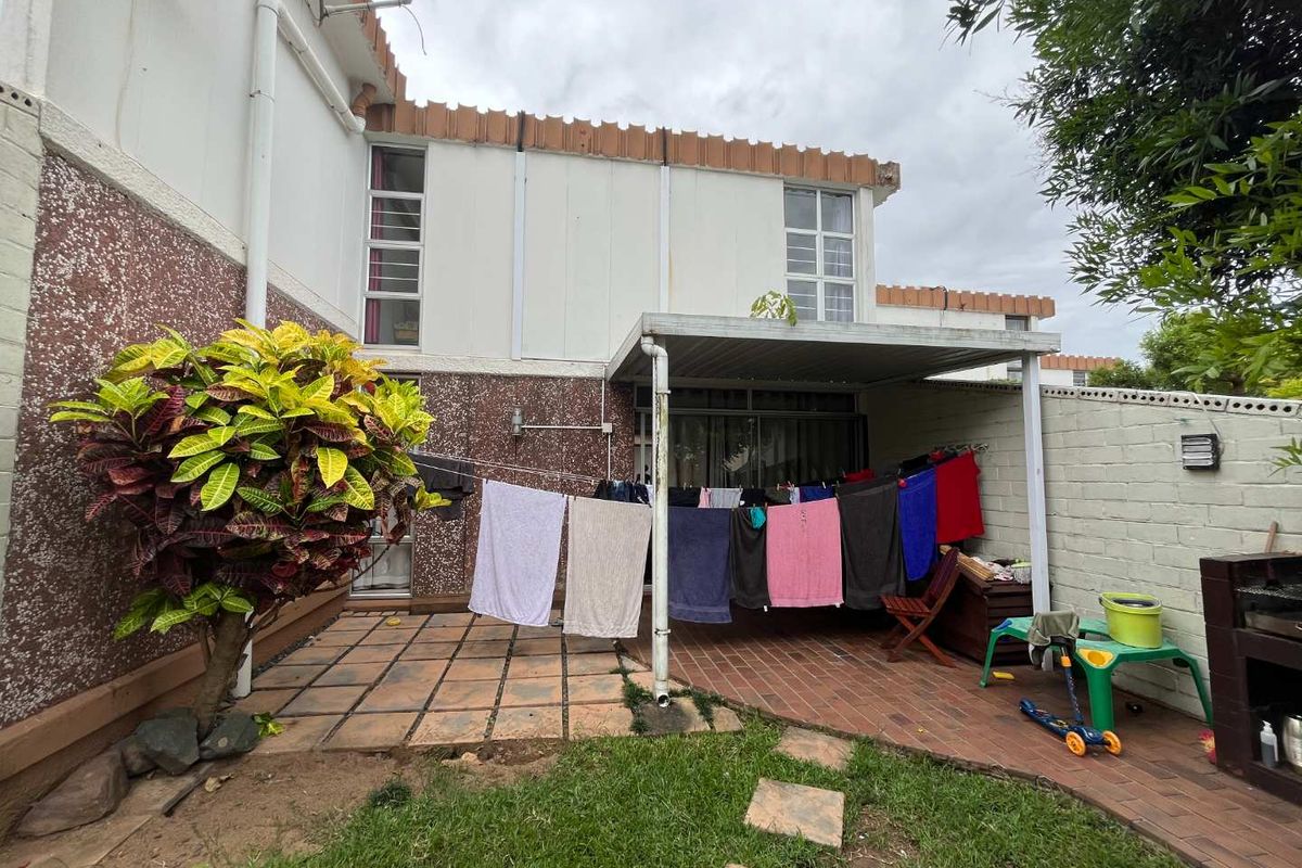 Rear exterior view of the townhouse featuring a covered patio area, paved flooring, and a small garden space.