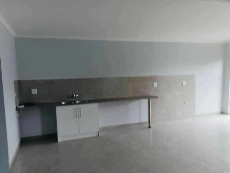 An open-plan living area featuring a minimalist kitchenette with built-in cabinetry, a sink, and neutral tiled flooring throughout.