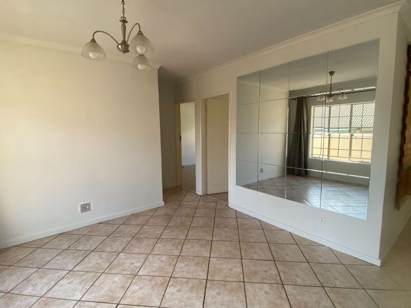 An empty living area featuring neutral tiled flooring, a large mirrored wall feature, and a classic ceiling light fixture.