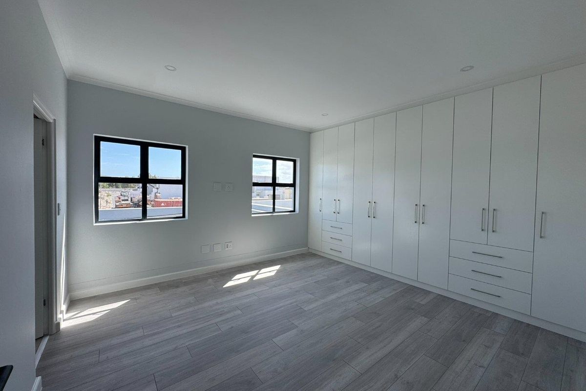 A bright, modern bedroom featuring light wood-look flooring, neutral walls, and extensive floor-to-ceiling built-in cabinetry with ample storage space.