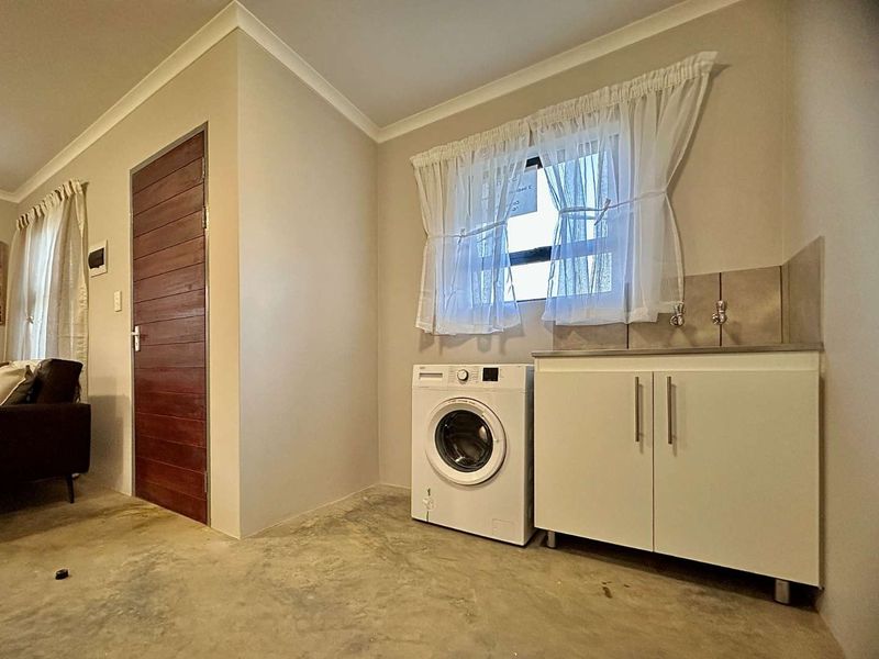 Functional laundry area featuring a built-in cabinet with sink, tiled splashback, and direct access via a timber door.