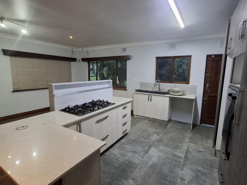 Modern kitchen featuring a central island with a gas hob, stone countertops, built-in oven, and ample cabinetry, finished with large format floor tiles.